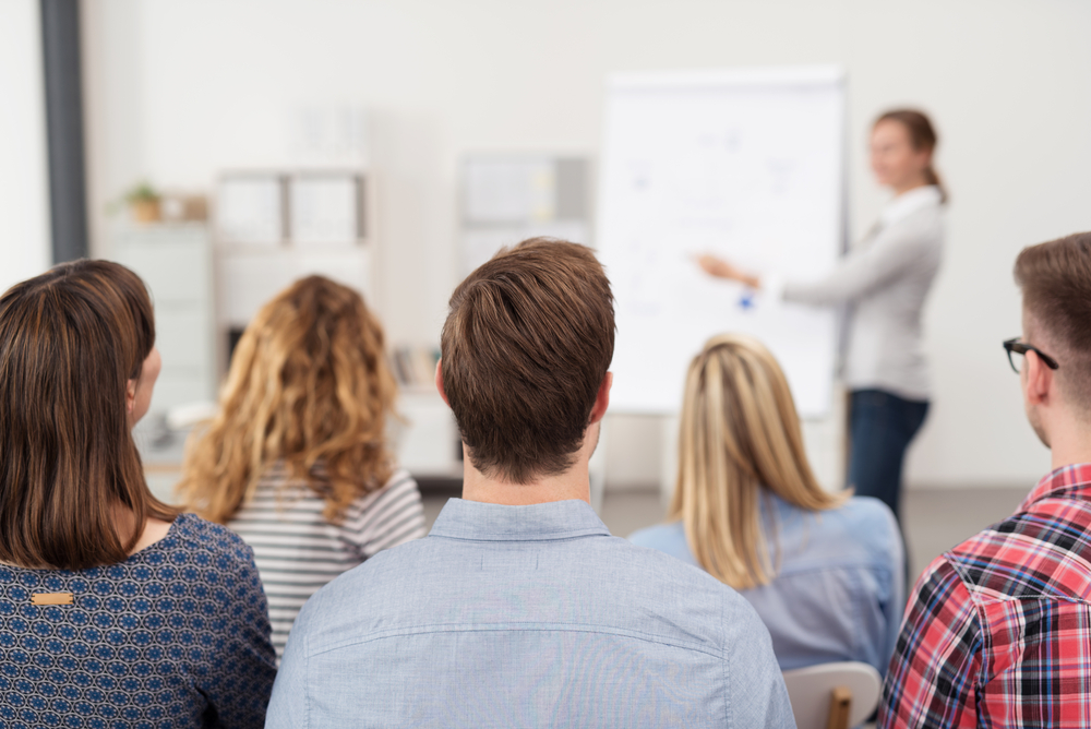 Rear View of Young Teachers in Casual Outfits Listening to a Top Manager Explaining Something Using Illustrations.